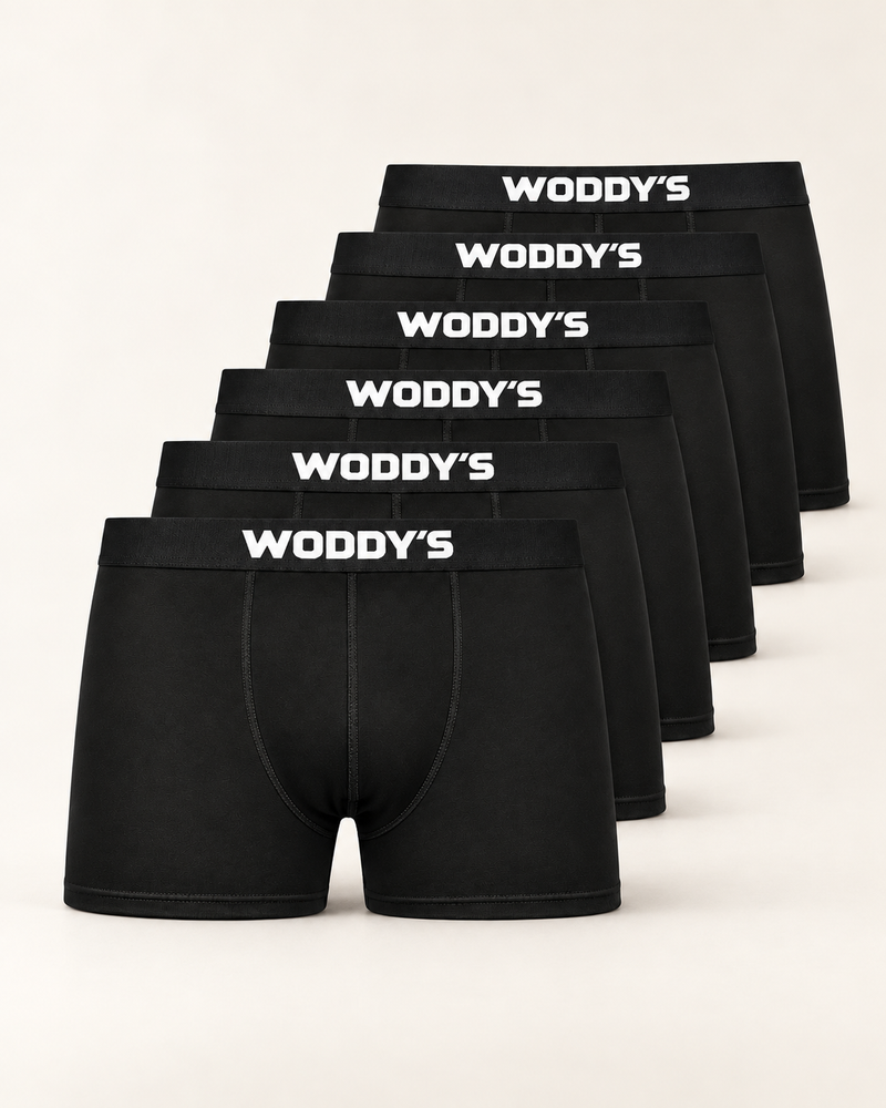 Sechs schwarze Boxershorts mit kurzem Bein und weißem WODDY’S-Logo, versetzt vor warmem Off-White.