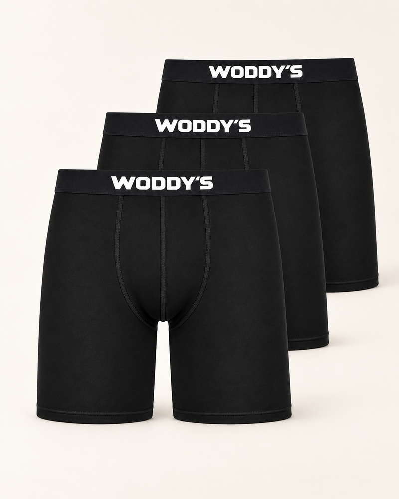 Drei schwarze Boxershorts mit langem Bein und weißem WODDY’S-Logo, versetzt vor warmem Off-White.